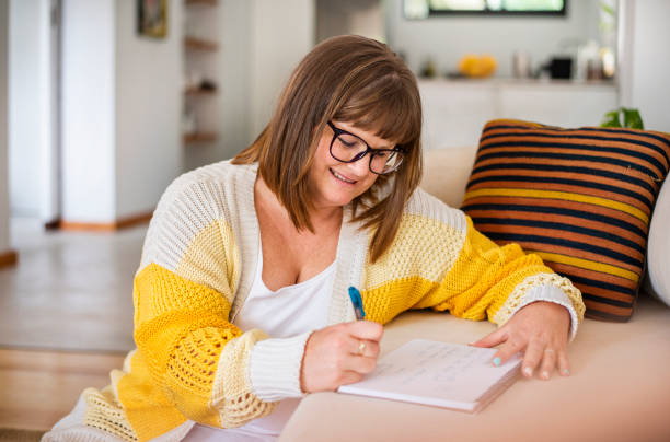 istock Smiling woman writing in a note pad on her living room sofa 1357751642