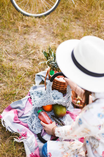 istock Young lady in white hat sitting on picnic blanket with string ba 1357753366
