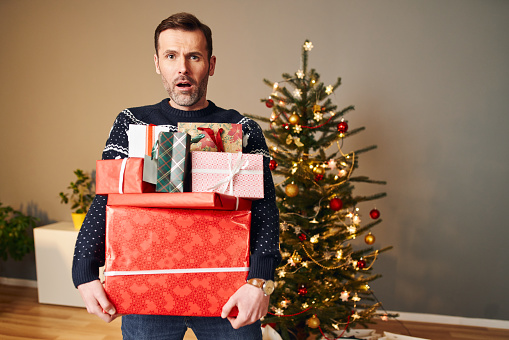 Overwhelmed mid adult man holding stack of heavy Christmas presents