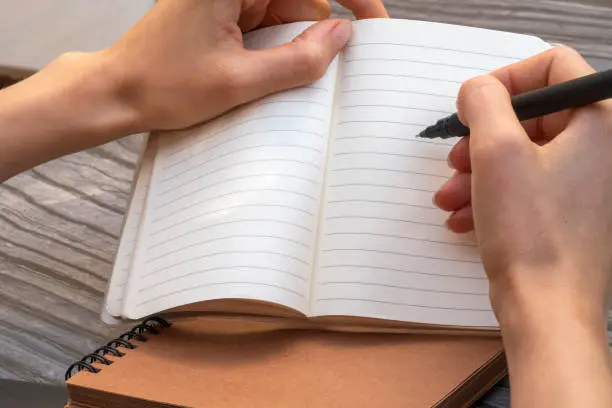 Empty open notebook with lined paper. Woman's hands taking notes with a black liner pen