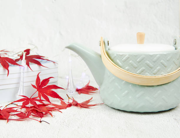 istock Light green tea pot with red maple leaves and books on a white background. Text space. 1357757970