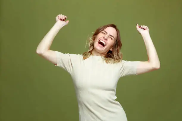 Photo of Overjoyed successful young woman celebrating win with raised arms, screaming with euphoria, happiness. Fortune concept