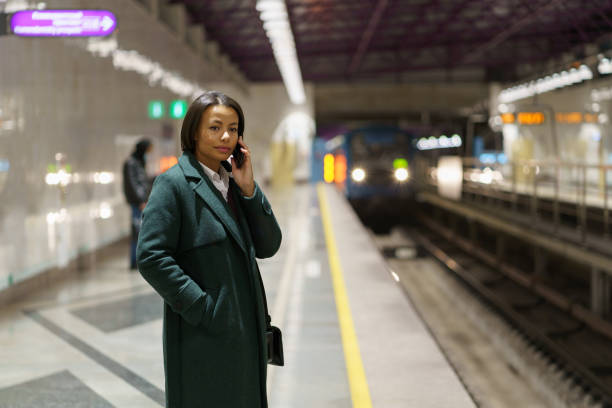 istock Young african american woman making mobile phone call while waiting for train at subway platform 1357764275