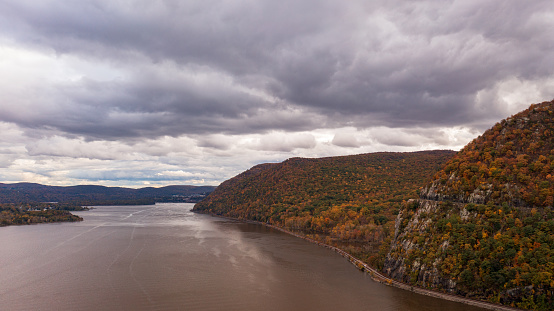 It is a cloudy day but the colorful fall foliage is still beautiful on the mountainside, upstate New York. The mountain is near the Hudson River. The dramatic shot was taken with a drone camera.