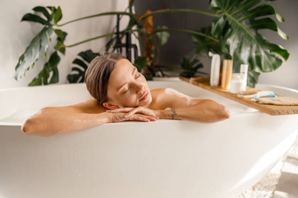 joven de ensueño apoyada en un lado de la bañera, relajándose con los ojos cerrados en casa - bathtub women naked human face fotografías e imágenes de stock