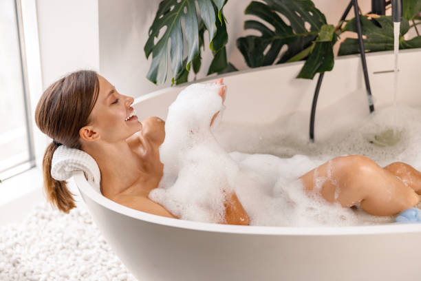 istock Bathing young woman relaxing in bath, smiling and playing with bubble foam 1357768847