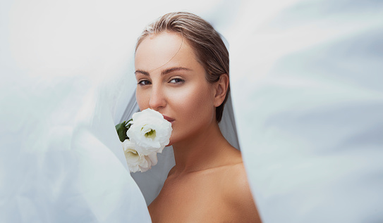 Beautiful young woman smelling a white flower under a white cover.