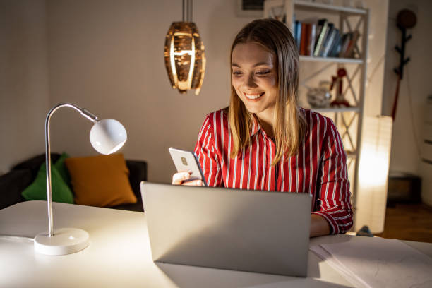 istock Young woman using mobile phone while working on the laptop 1357771333