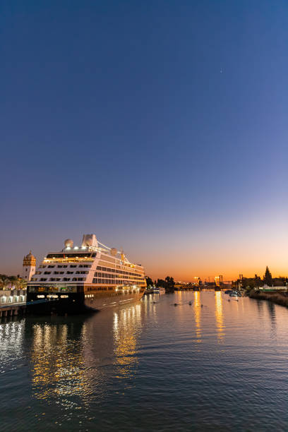 The Guadalquivir river at sunset, Seville, Spain. December, 2021. Seville, Spain. A river in the last rays of the sun with an iluminated cruise ship, small row boats and bridge in the distance. seville port stock pictures, royalty-free photos & images