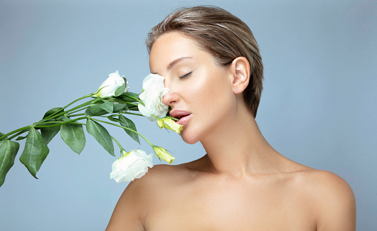 Portrait of beautiful woman with clean skin. She is smelling flower.