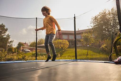 happy family are jumping on trampoline at backyard of their cozy home at summer sunset