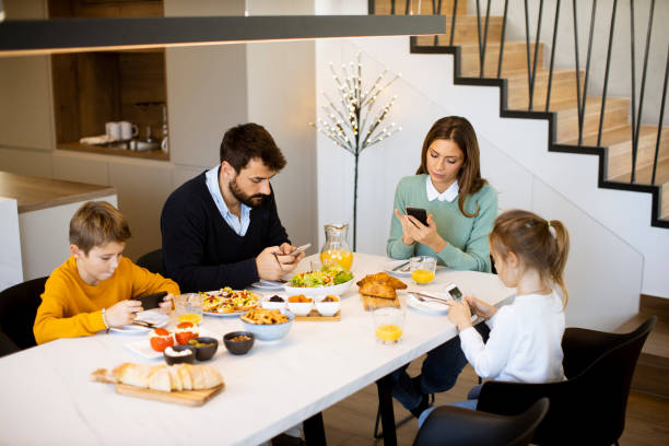 Family using mobile phones while having breakfast at dining table at apartment stock photo