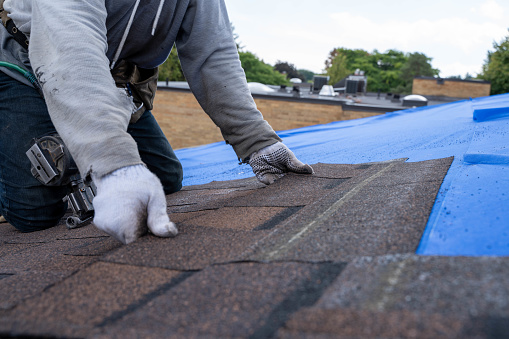 A roofer nails shingles over ridge vent material used on the peak of new residential house construction.