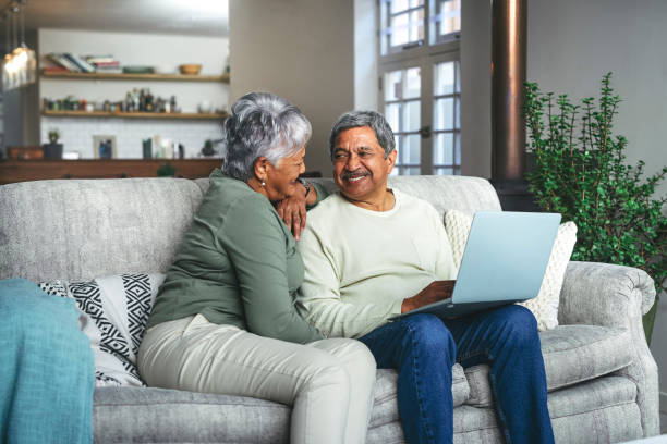 снимок пожилой пары, использующего дома ноутбук на диване - senior adult couple computer retirement стоковые фото и изображения
