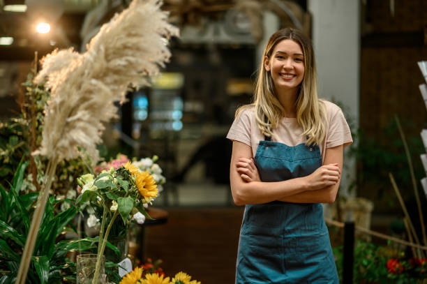 Florist working in flower shop while smiling and looking at a camera Portrait of beautiful florist working in flower shop while smiling and looking at a camera retail occupation photos stock pictures, royalty-free photos & images