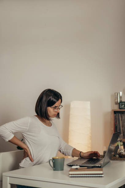 istock Beautiful woman having back and neck pain while using a laptop at home 1357786335