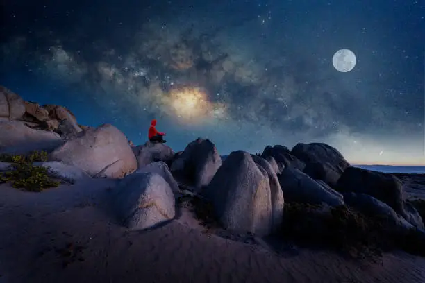 person sitting on the top of the mountain meditating or contemplating the starry night with Milky Way and Moon background in Atacama Desert