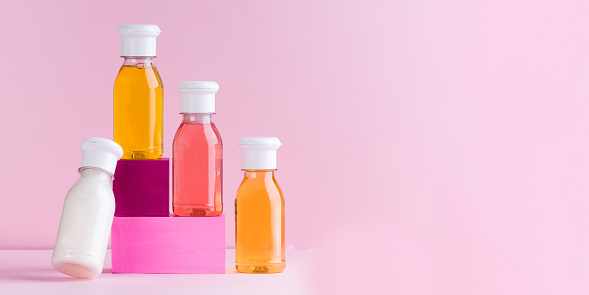 Mockup multicolored plastic bottles with shower gel, shampoo for children and adults on a pink background. Copy space. High quality photo