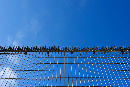 Low angle view of security wire fence against blue sky with copy space.