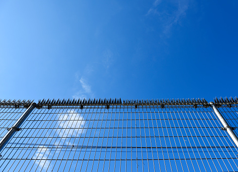 Low angle view of security wire fence against blue sky with copy space.