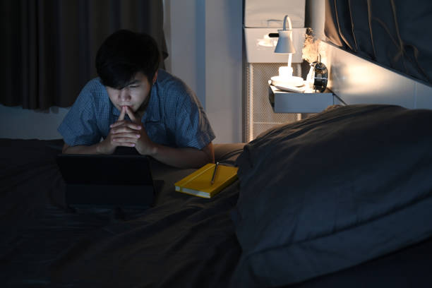 istock Man sitting in bedroom and using computer tablet at late night. 1357813109