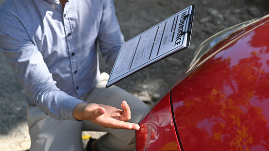 Agente de seguros de tiro recortado que sostiene el formulario de reclamo de seguro e inspecciona el automóvil dañado. photo