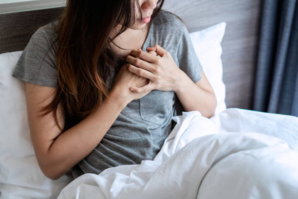 Young Asian woman suffering from heart attack in bedroom stock photo