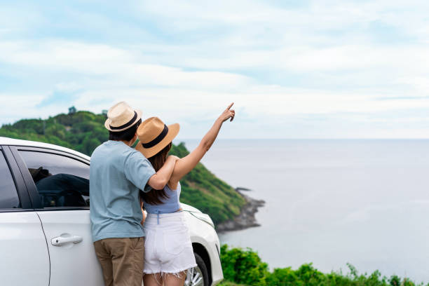 Young couple traveler looking at the beautiful sea view with their car while travel driving road trip on vacation stock photo