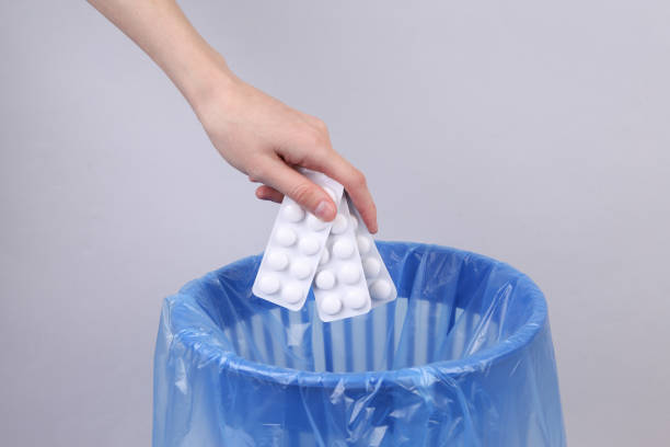 Hand throws blister pills into trash bin with package on gray background