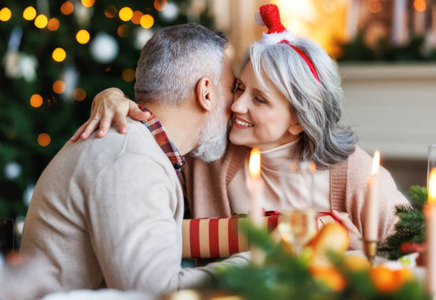 自宅でお祝いの夕食中にクリスマスプレゼントを抱きしめたり交換したりする幸せなシニアファミリーカップル - husband wife couple senior adult ストックフォトと画像