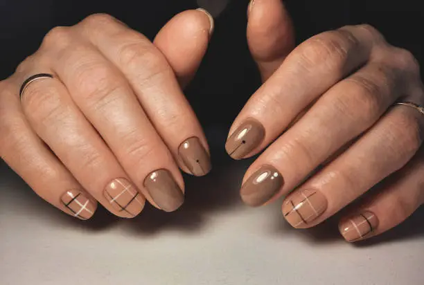Women's short nails with brown gel polish and black design. Brown nails with a checkered design.