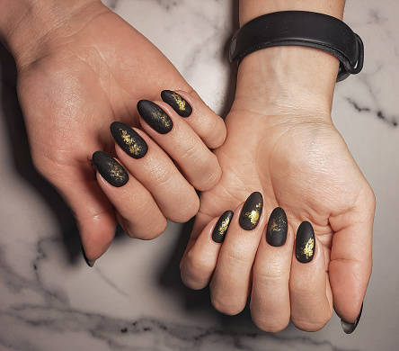 Women's manicure with a stylish, strict gel polish with a golden design. Black matte nails with gold sequins.