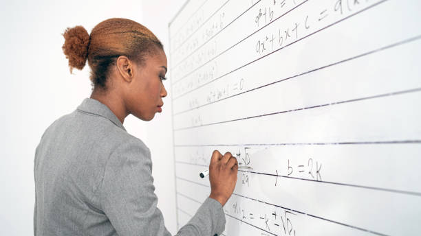 istock An African female teacher in an empty classroom writing on whiteboard 1357823176