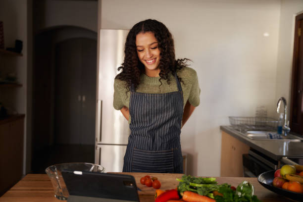 istock Multi-cultural young female reading recipe from tablet while cooking in modern kitchen. Fresh fruit and vegetables 1357823537