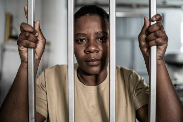 istock Young afro woman looking  serious and desperate   behind bars which may be prison bars or those of a security gate 1357823645