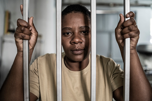 Young afro woman looking  serious and desperate   behind bars which may be prison bars or those of a security gate