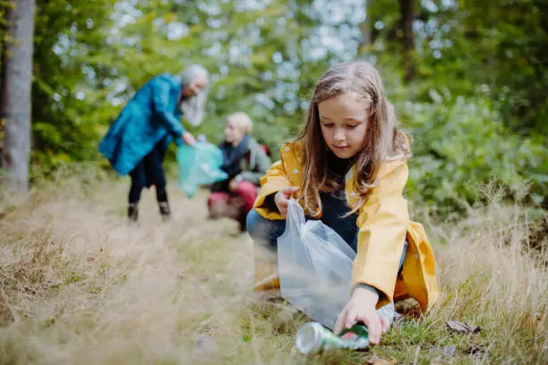 Photo of Small girl with mother and grandmother picking up waste outoors in forest.