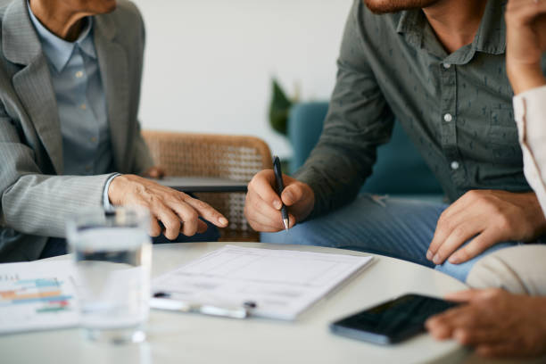 Close-up of couple signing contract with insurance agent in the office. Close-up of couple closing a deal with their financial advisor and signing paperwork during the meeting. life insurance stock pictures, royalty-free photos & images