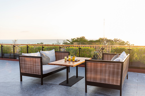 A cozy outdoor dining table with soft pillows and couches on a sunny day with a field background, horizontal.