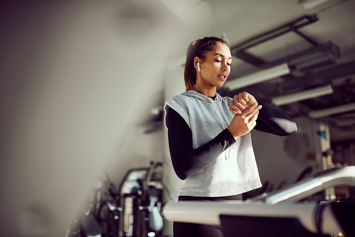 Young athletic woman using smartwatch while working out on treadmill at health club.