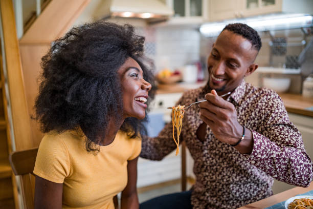 istock Shot of a young multiracial couple sharing spaghetti during a romantic dinner at a small living room 1357825334