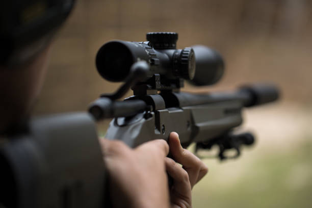 снайпер стреляет из винтовки, глядя через прицел. - rifle стоковые фото и изображения