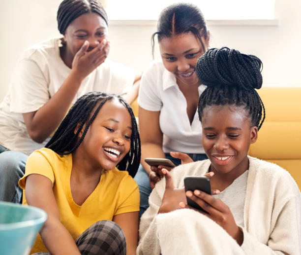 Group of teenage girls looking at photos on phone and smiling at home stock photo
