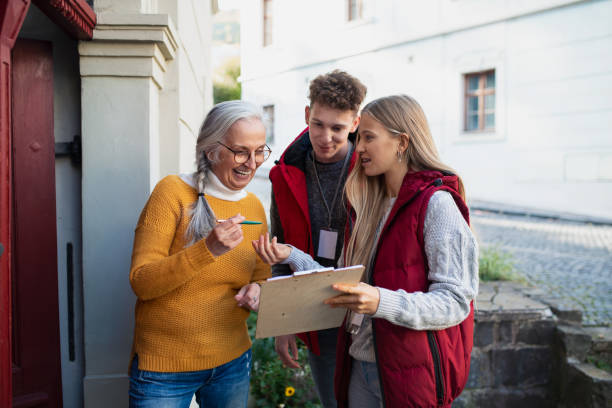 Young door to door volunteers talking to senior woman and taking survey at her front door. Young door to door volunteers talking to senior woman and taking a survey at her front door. charitable foundation stock pictures, royalty-free photos & images