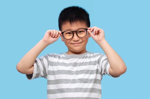 Kid wearing glasses and tshirt, taking eyesight test on blue background