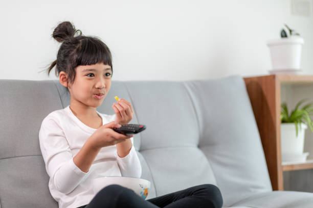 istock Kid with remote control sitting on the couch watching a movie on tv 1357828699