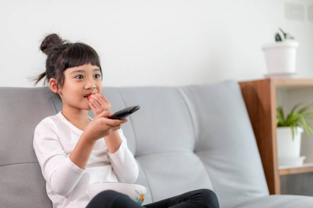 istock Kid with remote control sitting on the couch watching a movie on tv 1357828700
