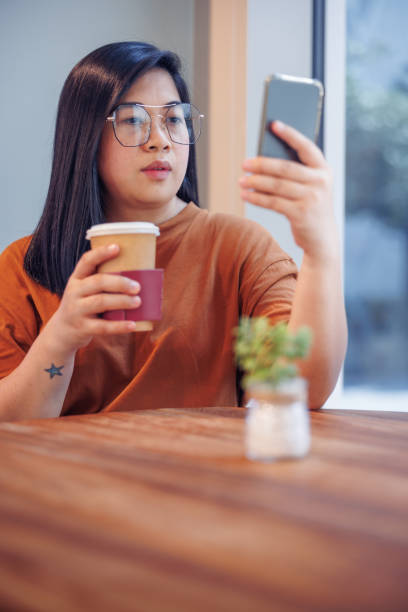 istock Young woman with eyeglasses using mobile phone for video call in cafeteria 1357833932
