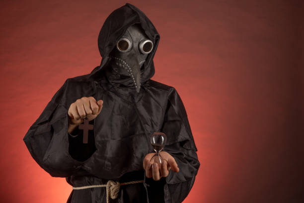 A man dressed as a plague doctor holds an hourglass and a crucifix in his hands A man dressed as a plague doctor holds an hourglass and a crucifix in his hands black plague doctor stock pictures, royalty-free photos & images