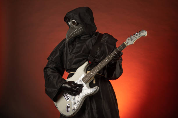 A man in a plague doctor costume plays the guitar emotionally on a red background A man in a plague doctor costume plays the guitar emotionally on a red background black plague doctor stock pictures, royalty-free photos & images